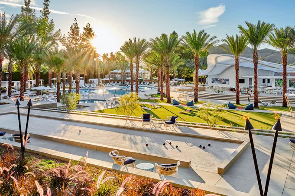 Resort grounds with palm trees, pool area, bocce ball court, and modern white buildings