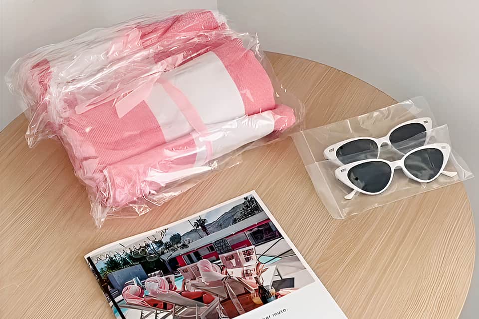 Pink and white striped beach bag, white heart-shaped sunglasses, and tropical resort photo on wooden surface