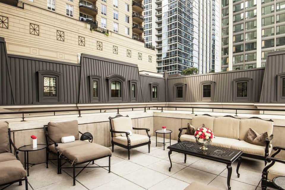 Urban rooftop terrace with cushioned seating, metal railings, and city buildings backdrop