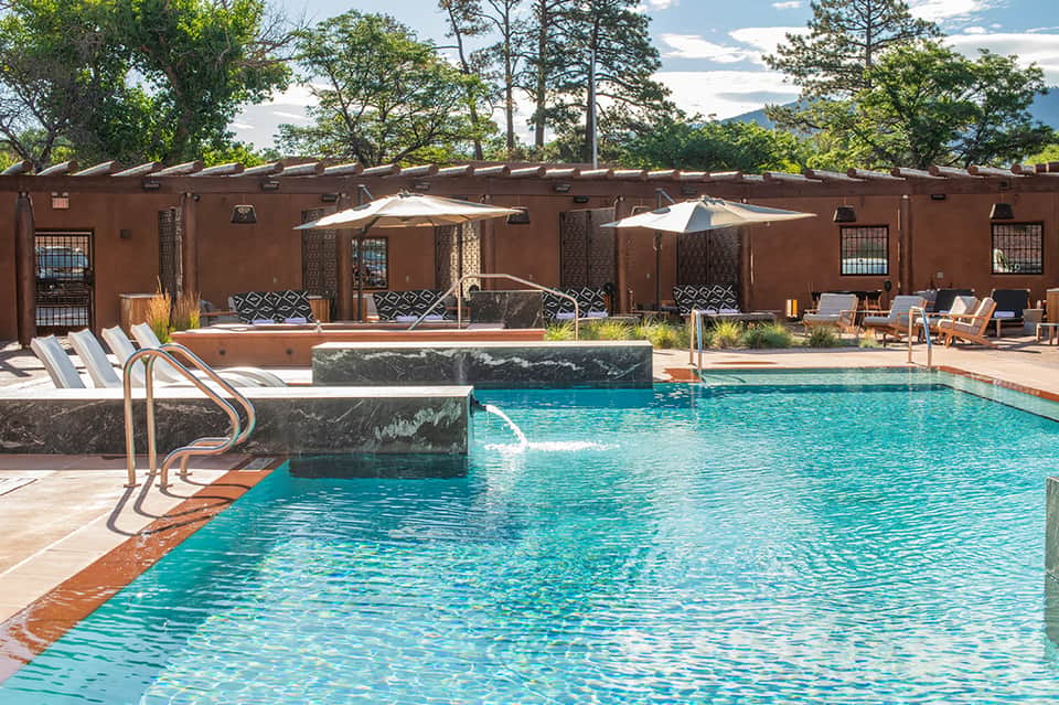 Resort pool with terracotta walls, lounge chairs, umbrellas, and mountain views