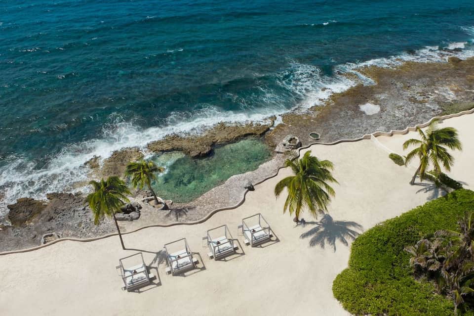 Aerial view of sandy beach with palm trees, lounge chairs, and turquoise ocean waves