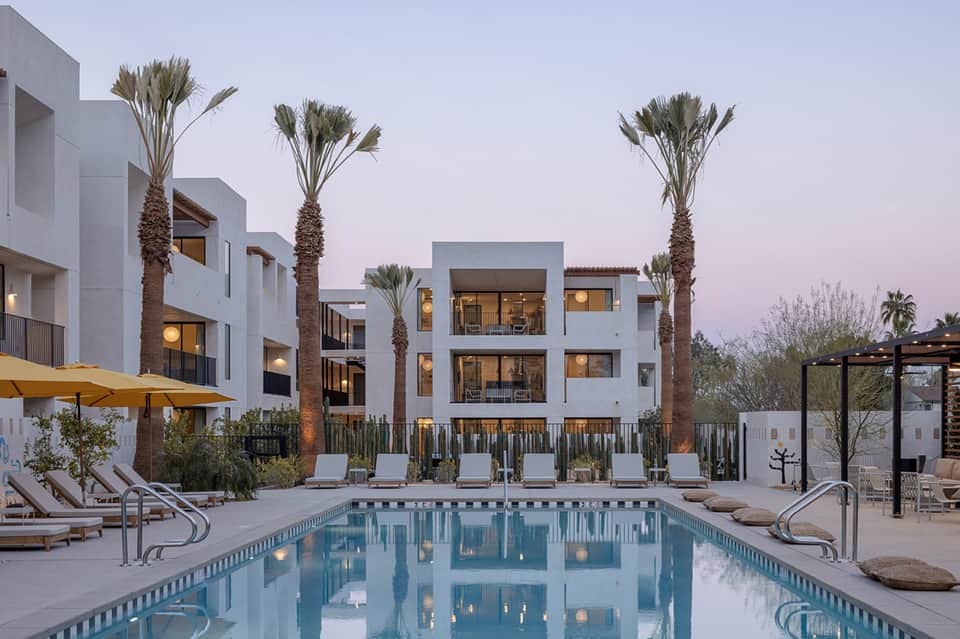 Modern white residential complex with palm trees and illuminated pool at dusk