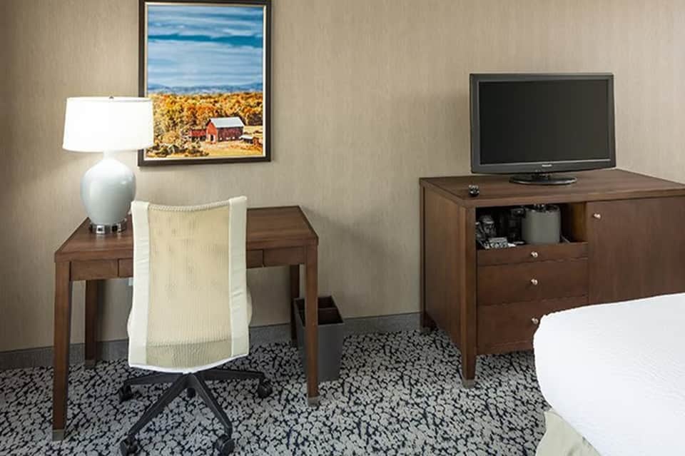 Hotel room with desk, TV stand, and framed landscape artwork