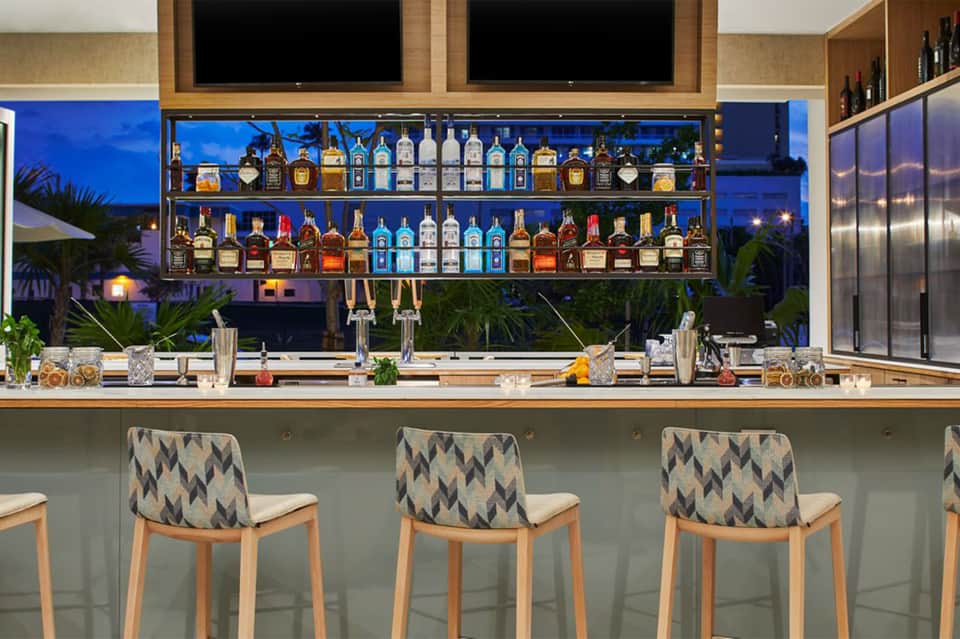 Upscale bar with illuminated liquor shelves, blue ambient lighting, and patterned bar stools