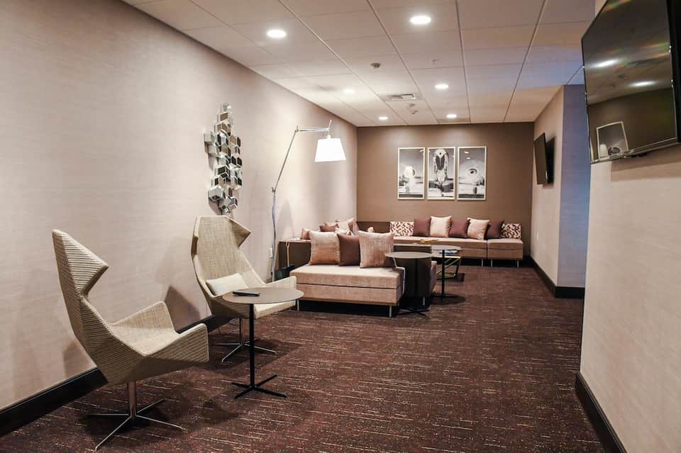 Contemporary hotel lounge with beige seating, brown accent wall, framed artwork, and flat-screen TV