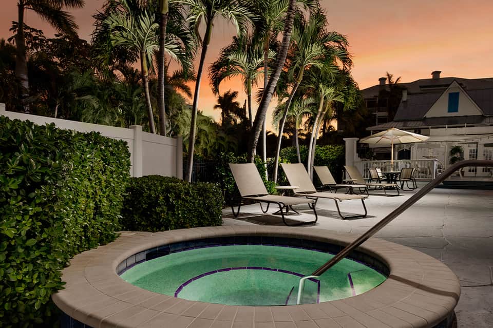 Spa hot tub at dusk surrounded by lounge chairs, palm trees, and modern residential architecture at sunset