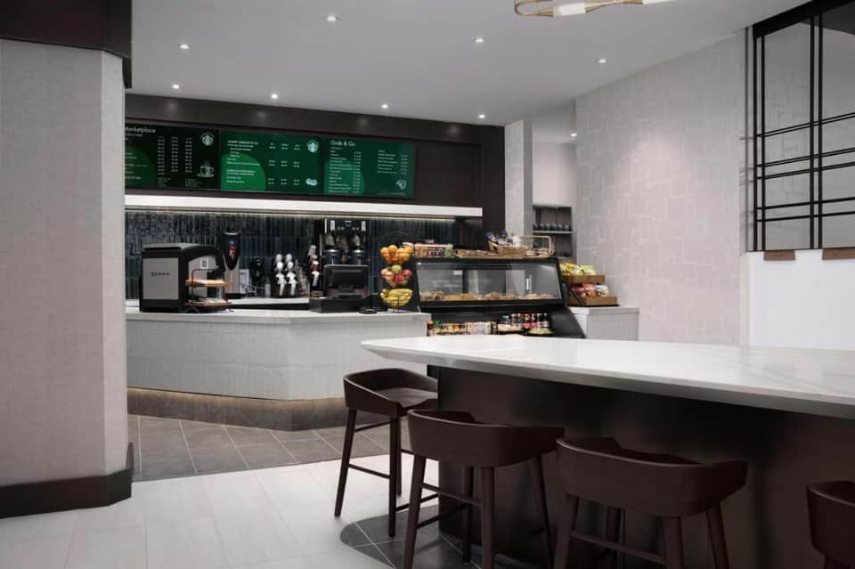 Modern Starbucks café interior with green menu boards, white counter, black bar seating, and contemporary lighting