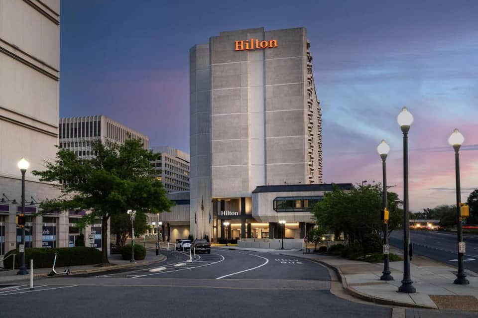 Hilton hotel exterior at dusk with illuminated signage, multi-story concrete tower, and street-level entrance