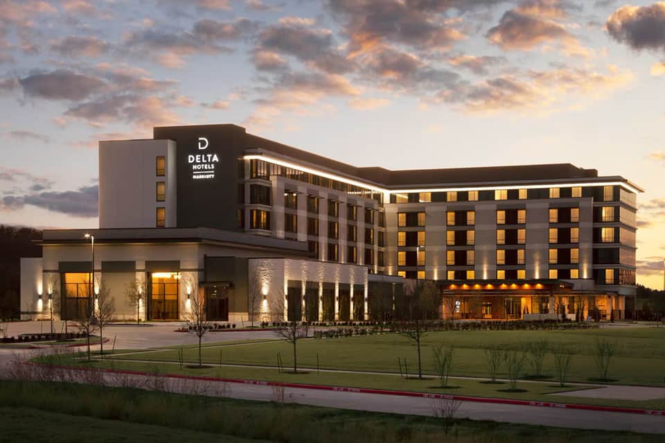 Modern Delta Hotels building exterior at dusk with illuminated windows and manicured landscape