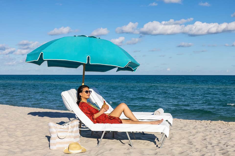 Woman in red dress relaxing under turquoise umbrella on white lounger with ocean view