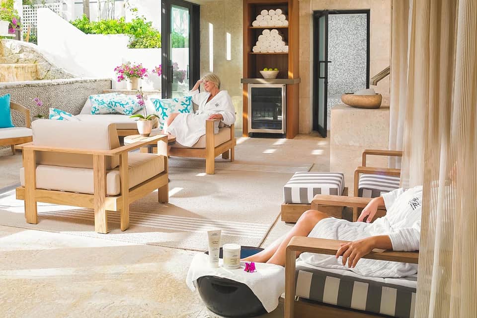 Spa relaxation area with wooden lounge chairs, turquoise pillows, and fireplace