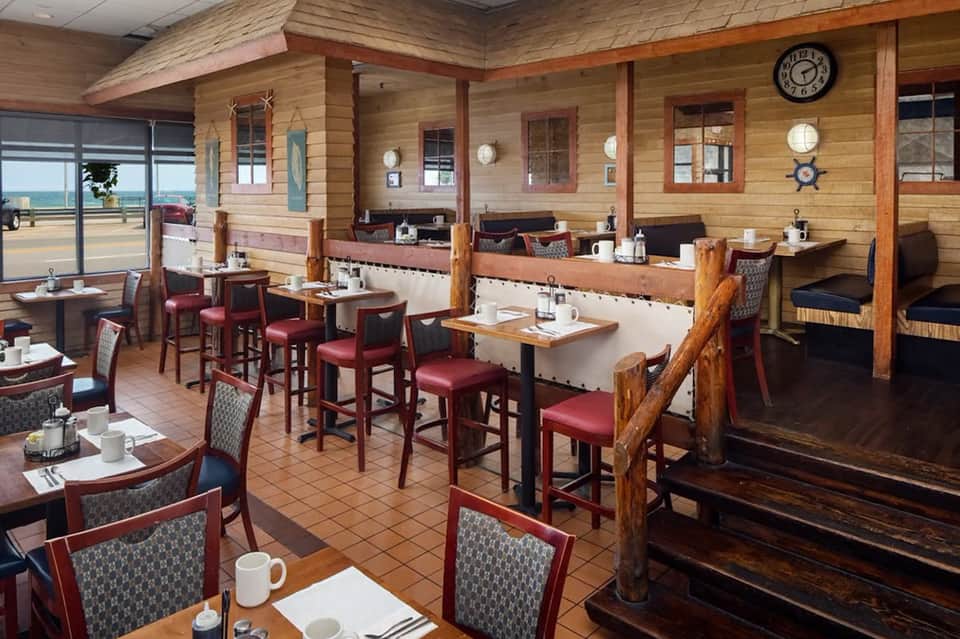 Nautical-themed restaurant with wood beam ceiling, red upholstered seating, ocean view windows, and maritime decor