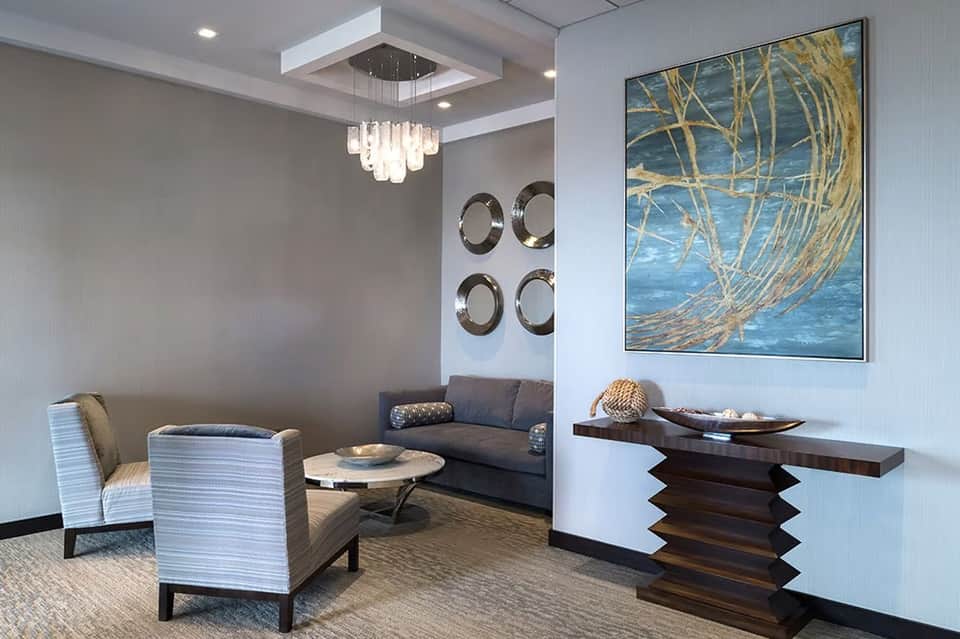 Modern hotel lounge with gray sofa, decorative mirrors, crystal chandelier, and abstract artwork
