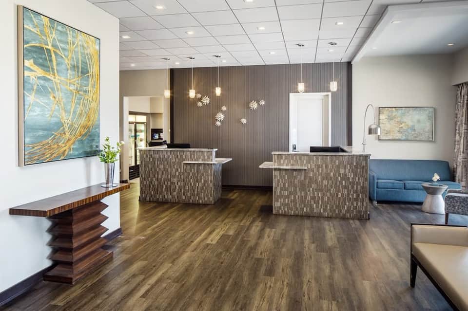 Hotel lobby with dual reception desks, patterned wall panels, pendant lighting, and contemporary furnishings