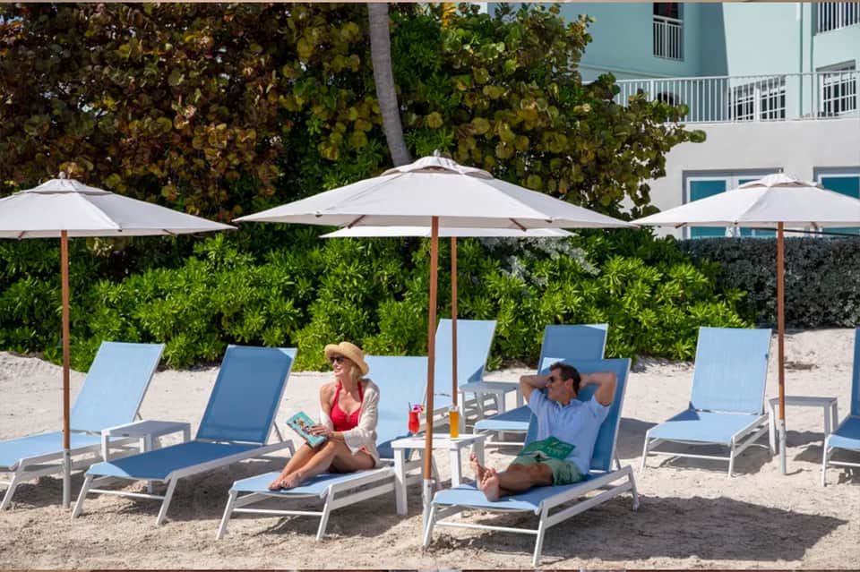 Beach lounge area with blue chaise lounges, white umbrellas, and tropical landscaping