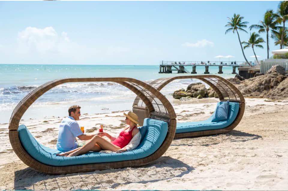 Couple relaxing in woven lounge chairs on beach with ocean and pier in background