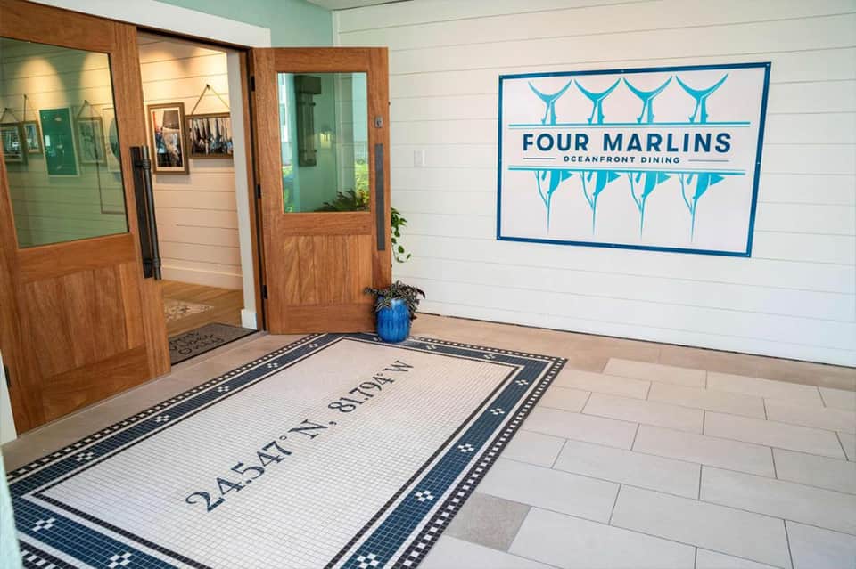 Modern hotel entrance with white tile flooring and blue Four Marlins oceanfront dining sign