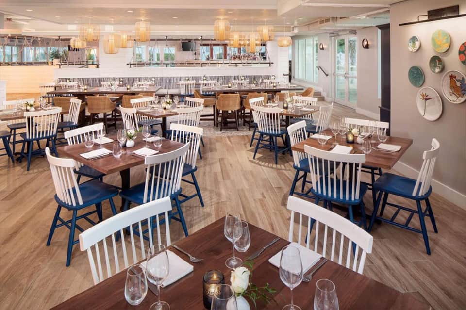 Upscale restaurant dining room with wooden tables, white and blue chairs, and pendant lighting