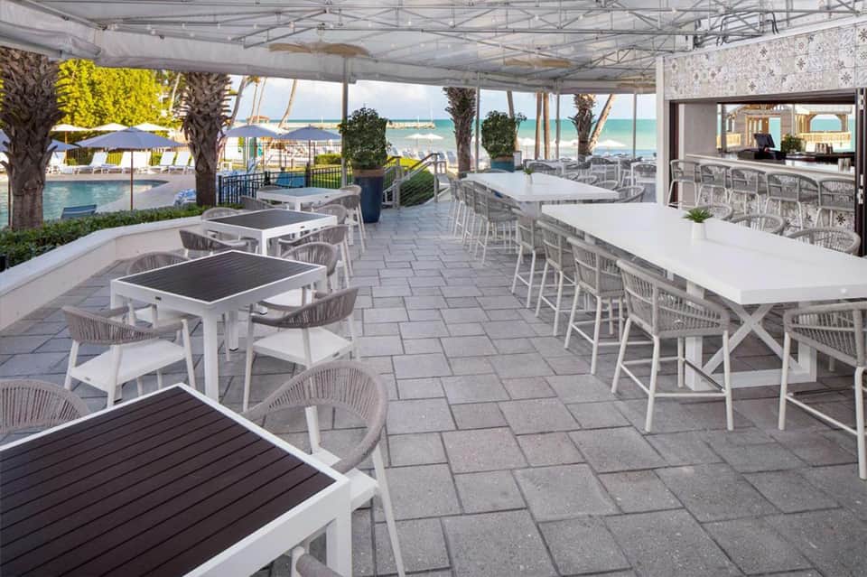 Modern outdoor dining pavilion with white tables and chairs overlooking pool and ocean