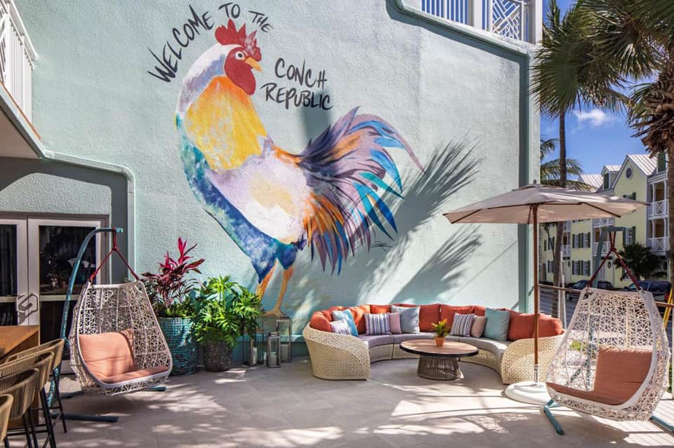Outdoor patio with colorful rooster mural, woven hanging chairs, curved seating, and umbrella