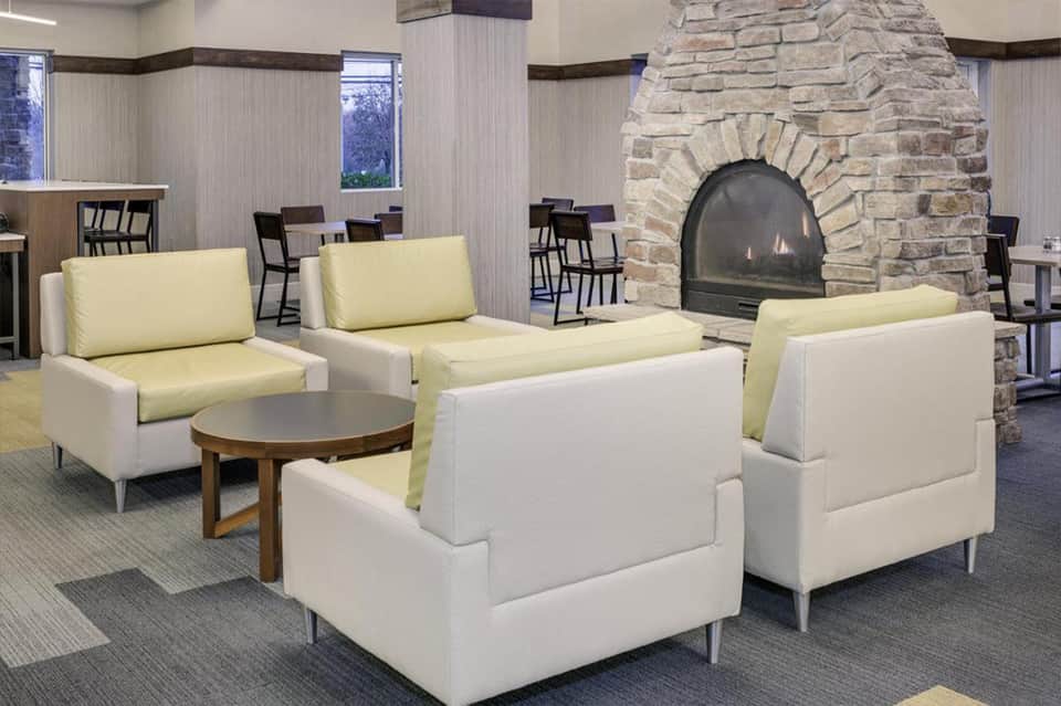 Modern lounge area with cream upholstered chairs, wooden side table, and stone fireplace with gas insert
