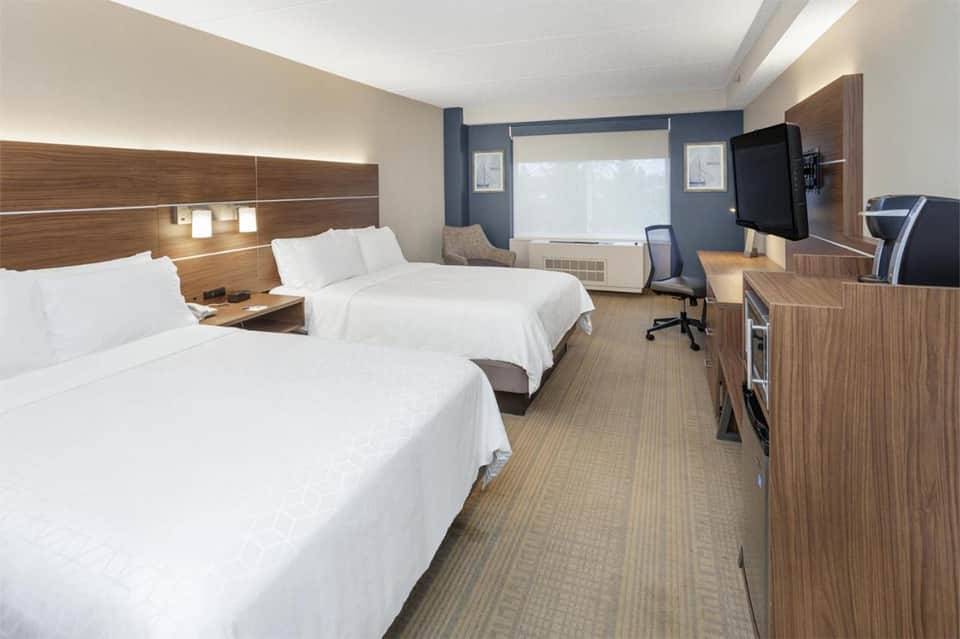 Modern hotel room with two queen beds, wood headboards, blue accent wall, and work desk