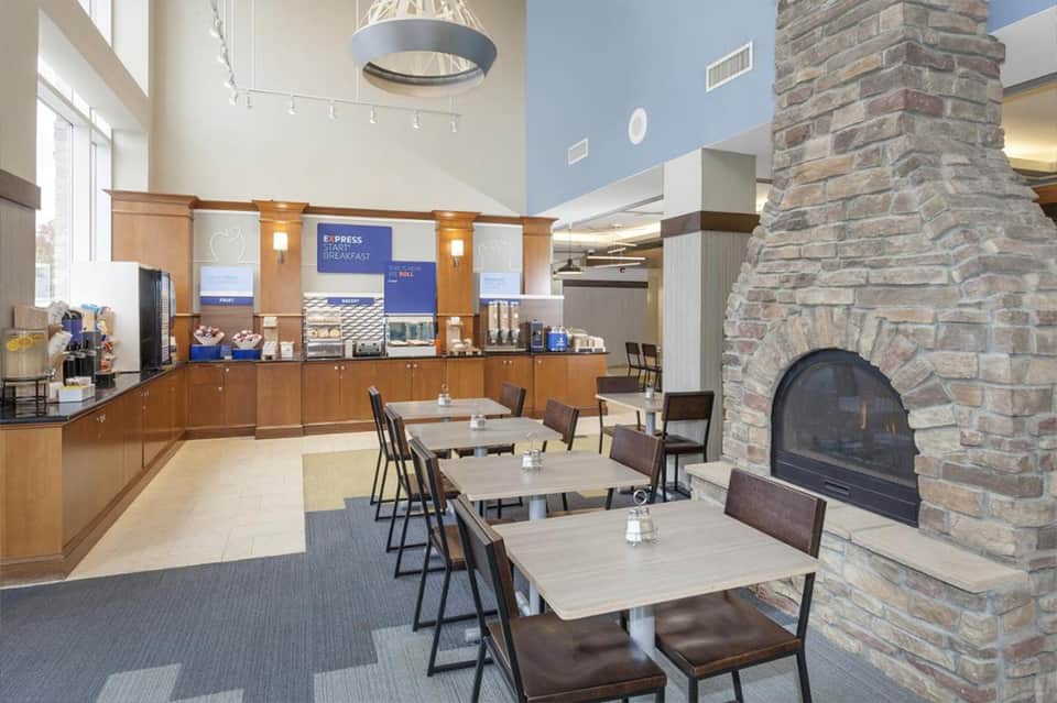 Hotel breakfast area with wooden counter, fireplace, and dining tables under high ceiling