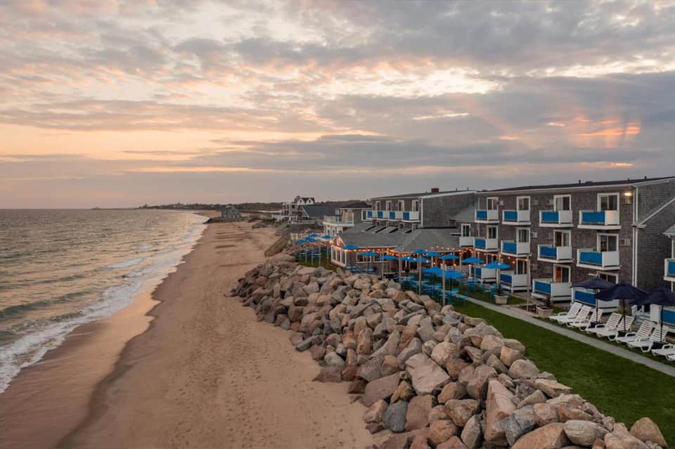 Beachfront resort at sunset with rocky seawall, sand beach, and multi-story blue-accented buildings