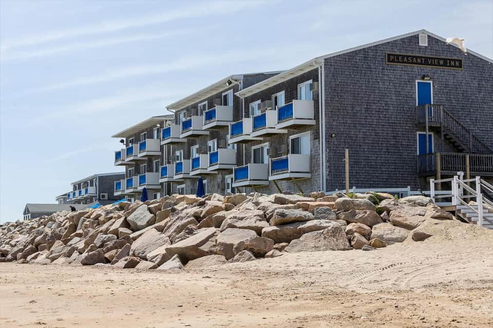 Pleasant View Inn beachfront building with blue balconies on sandy shore with boulder breakwater