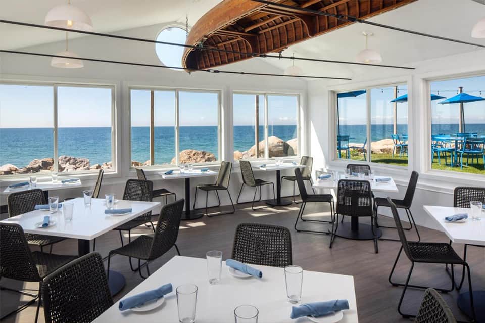 Modern beachfront dining room with floor-to-ceiling windows overlooking ocean and rocky coastline