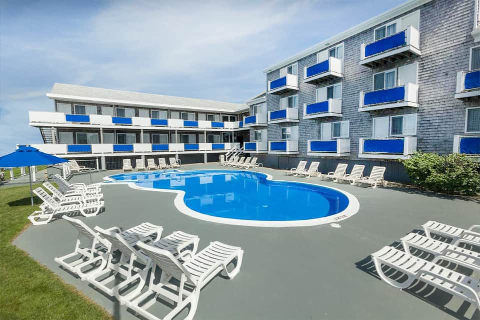 Large blue swimming pool with white loungers in front of beachfront hotel building