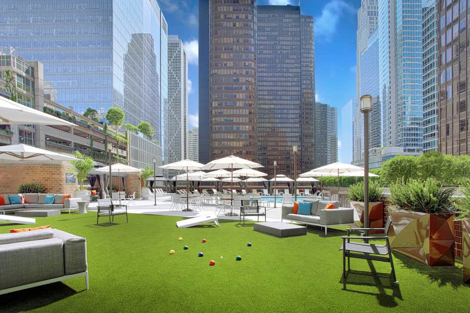 Urban rooftop lawn with white umbrellas, lounge seating, and Manhattan skyline backdrop