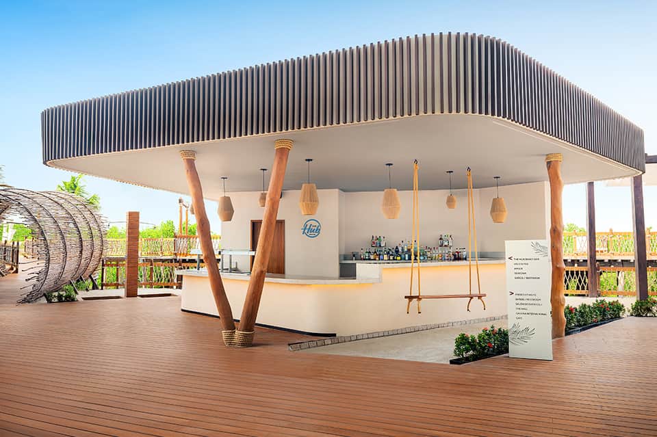 Modern outdoor bar pavilion with corrugated metal canopy, wooden support columns, and hanging pendant lights overlooking vineyard landscape