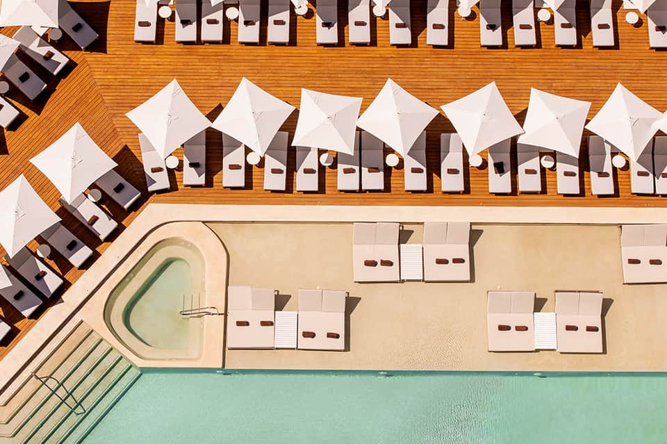 Aerial view of resort pool with lounge chairs and umbrellas on wooden deck