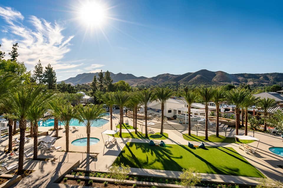 Resort courtyard with palm trees, pools, and mountain views under clear blue sky