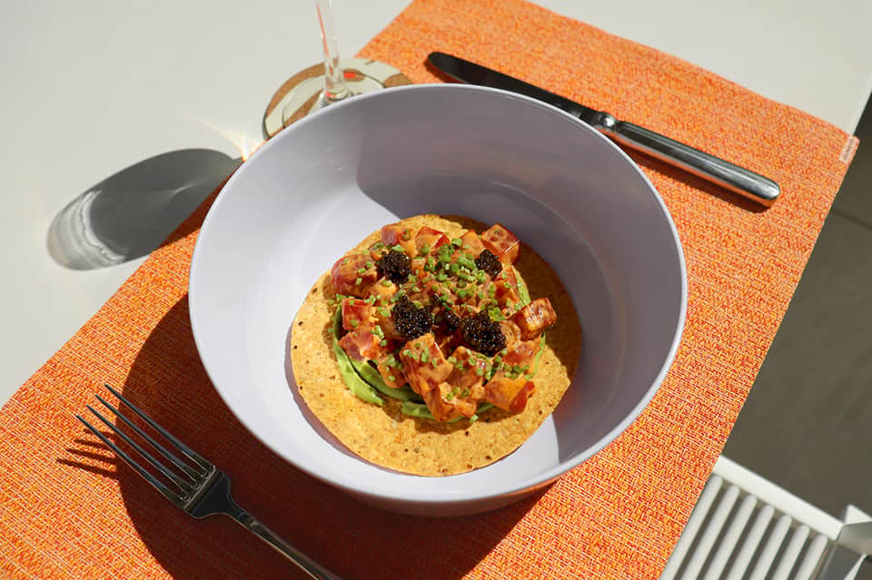 Gourmet dish with seared protein, colorful vegetables, and microgreens served in white bowl on orange placemat