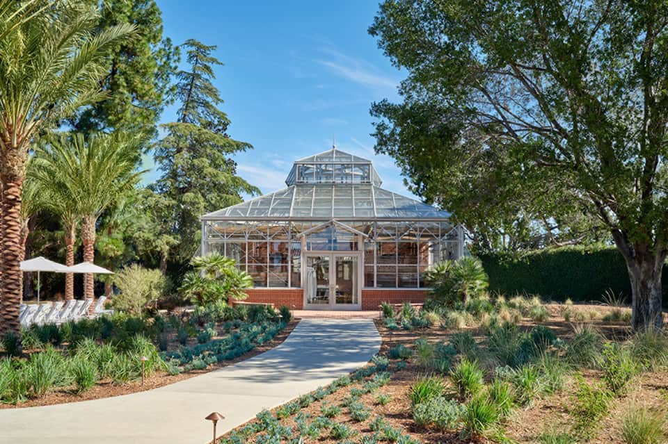Glass conservatory greenhouse with brick base surrounded by desert landscaping and palm trees