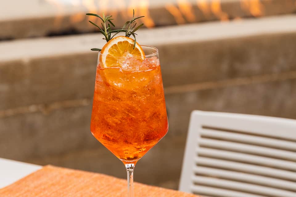 Orange cocktail with rosemary garnish and orange slice on poolside table