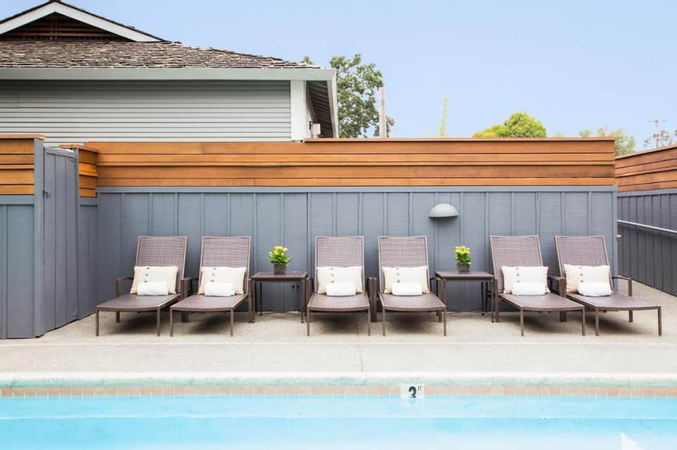 Row of lounge chairs with cushions beside residential pool and fenced yard