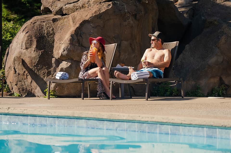 Two people relaxing in lounge chairs by pool with large boulder rock formation backdrop