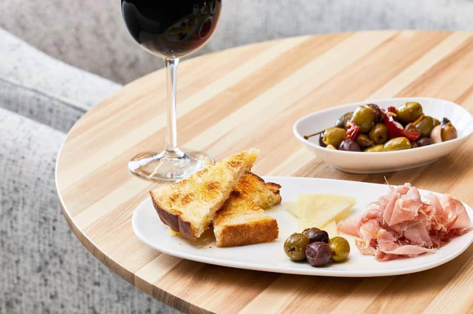 Wine glass, charcuterie board with cured meats, cheese, and olives on wooden table