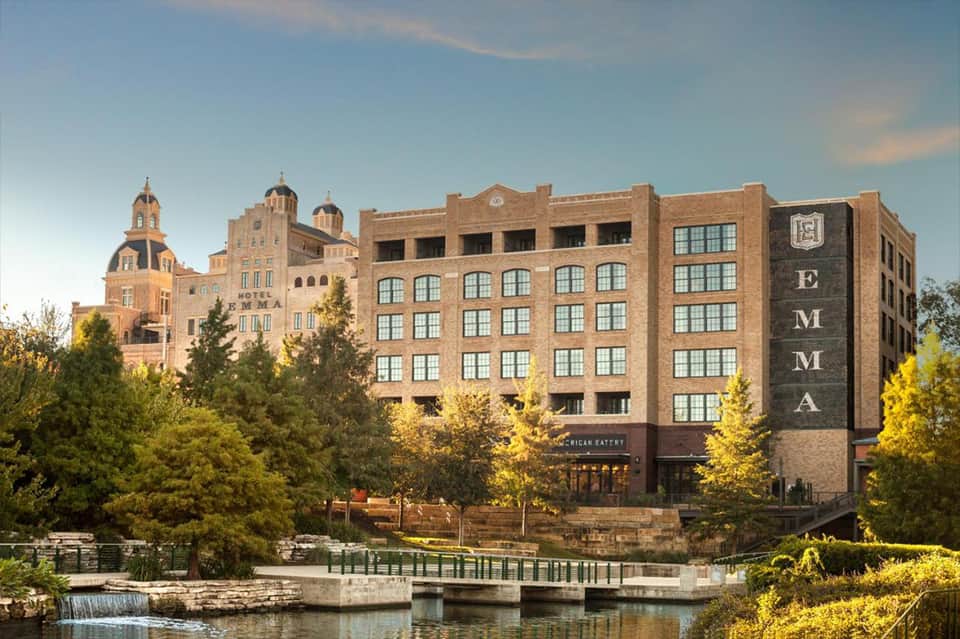 Historic brick hotel building with distinctive domed architecture beside a river with waterfall and green trees