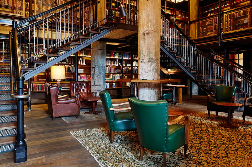 Multi-level library lounge with metal staircases, leather armchairs, and bookshelves