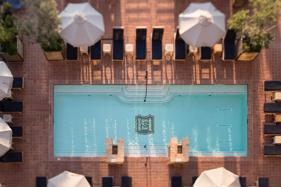Aerial view of rectangular pool with white umbrellas and lounge chairs on brick deck