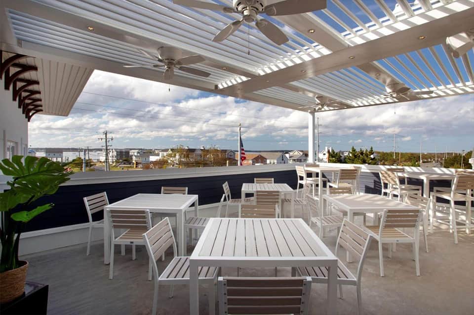 Rooftop dining area with white pergola, ceiling fans, tables, chairs, and waterfront views