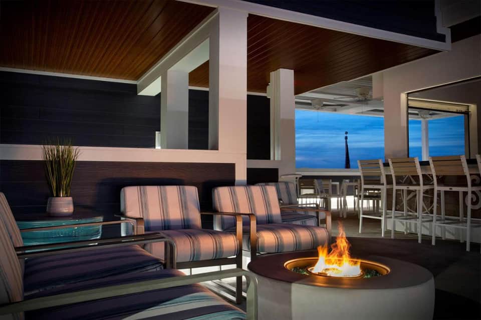 Oceanfront terrace with fire pit, striped seating, wooden ceiling, and blue water views at dusk