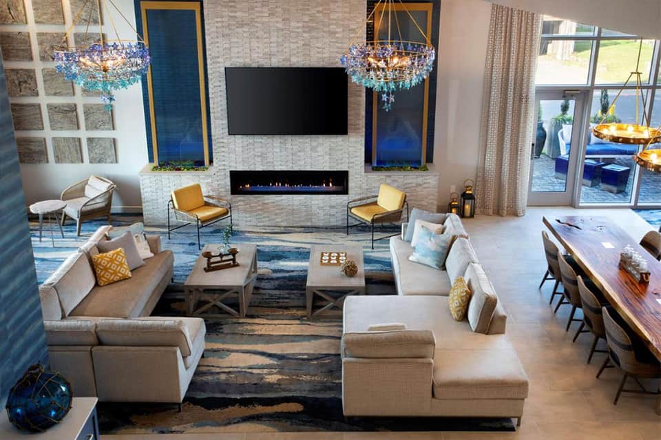 Luxury lobby with fireplace, white sofas, blue crystal chandeliers, yellow accent chairs, and contemporary design