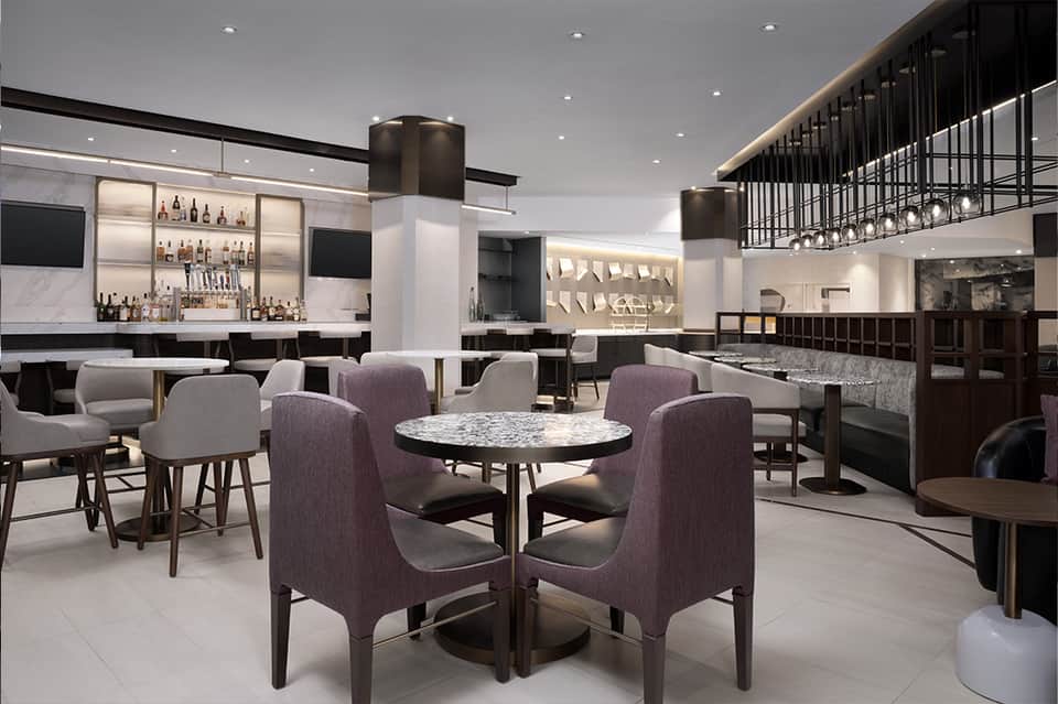 Modern hotel lounge with purple upholstered chairs, marble tables, and illuminated bar