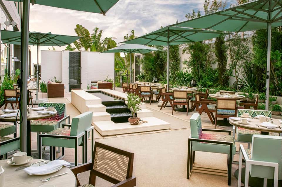 Outdoor restaurant terrace with green umbrellas, dining tables, and tropical plants
