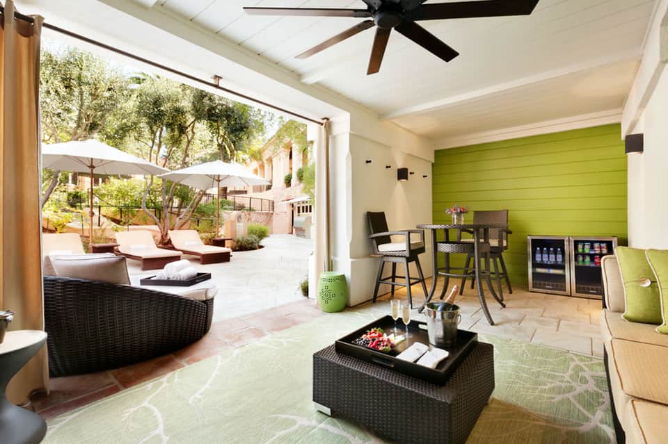 Modern lounge area with lime green accent wall, black wicker furniture, and open patio doors overlooking a resort courtyard.